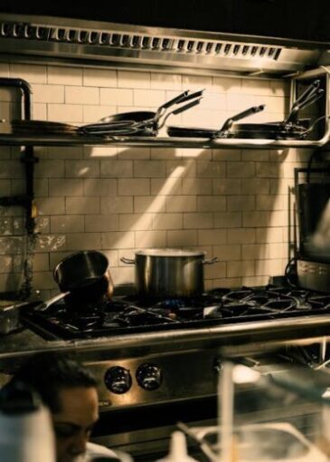 A well-equipped restaurant kitchen with pans and pots on a stove under warm lighting.